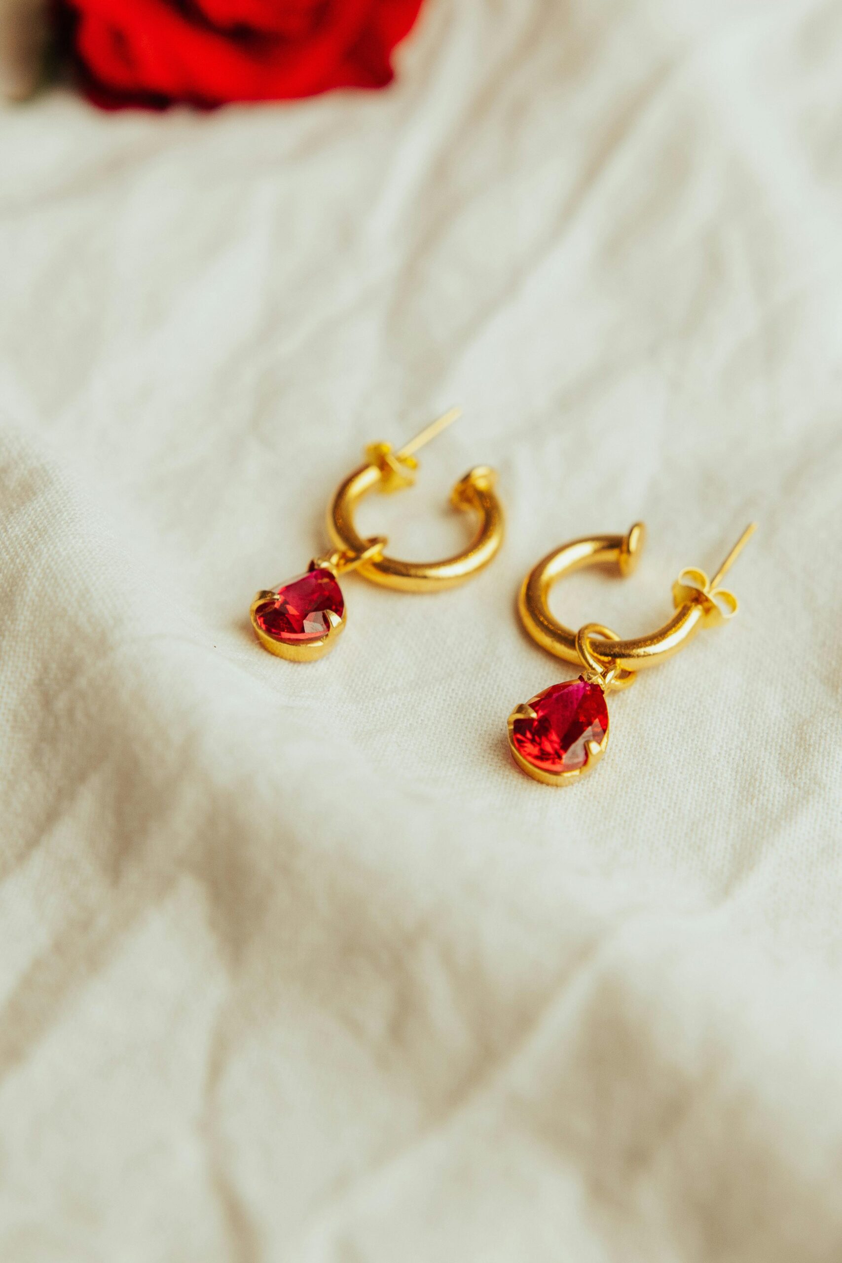 Close-up shot of gold earrings with red gemstones on white fabric, exuding luxury and elegance.