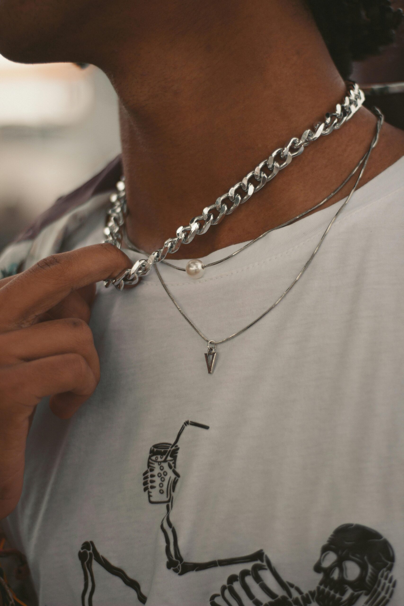 Stylish layered necklaces worn over a t-shirt with skeleton design, highlighting modern jewelry style.