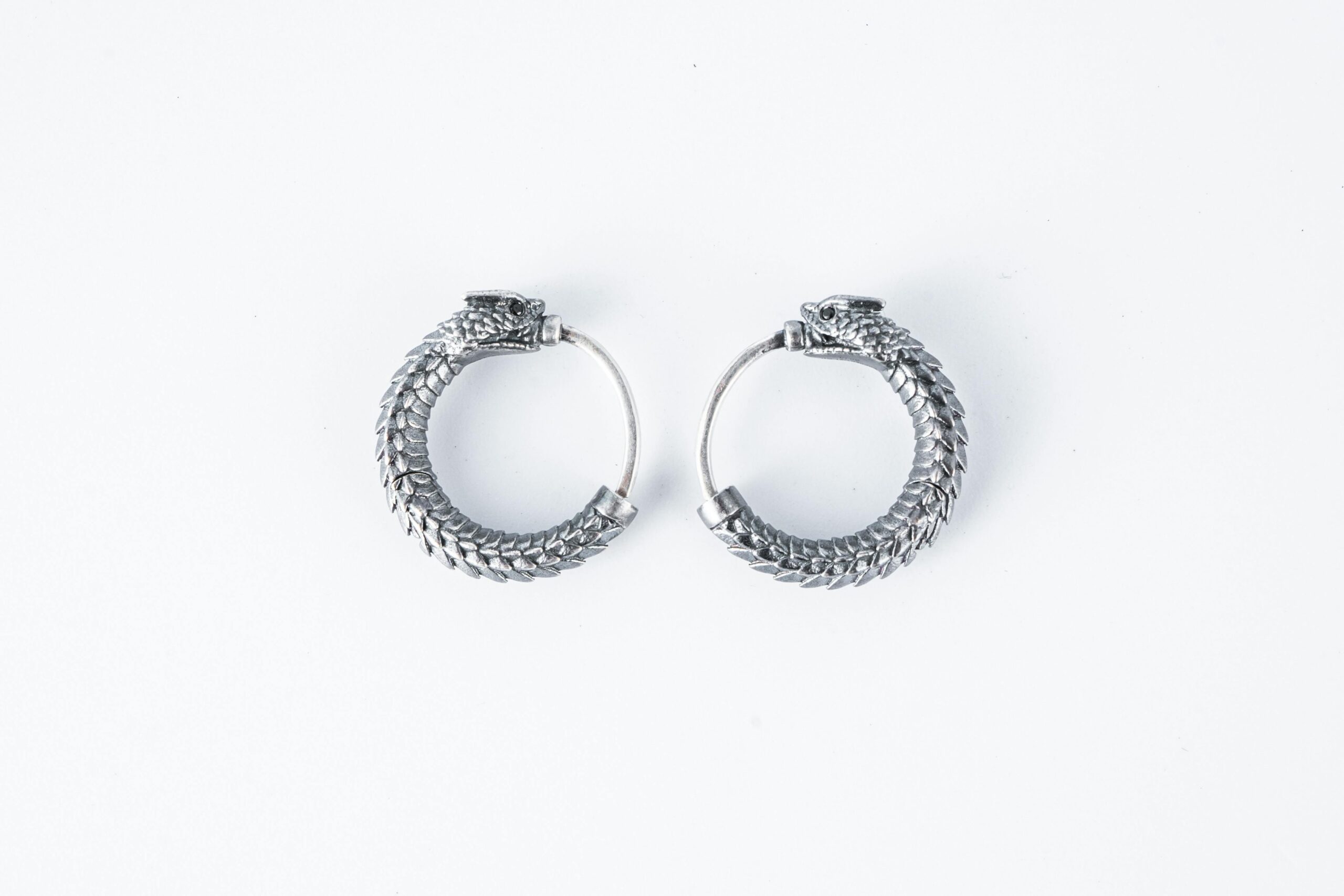 Close-up of intricate silver dragon-themed hoop earrings on a white backdrop.