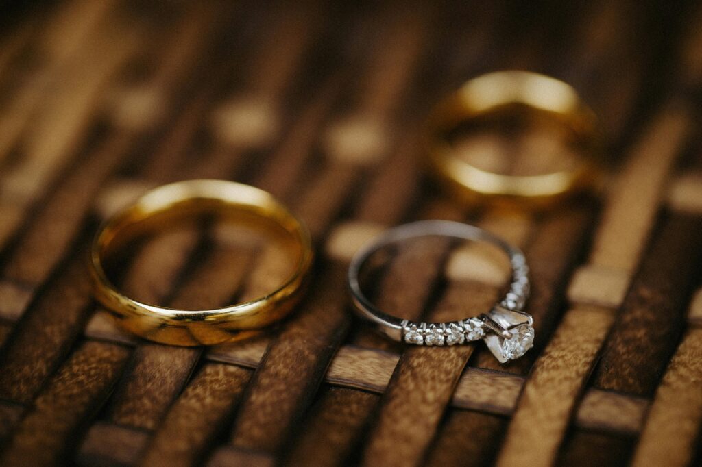 Close-up of wedding and engagement rings on woven surface, highlighting gold and diamonds.