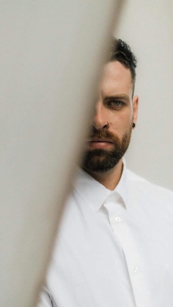 Side view portrait of a man with a beard looking serious in a white shirt indoors.