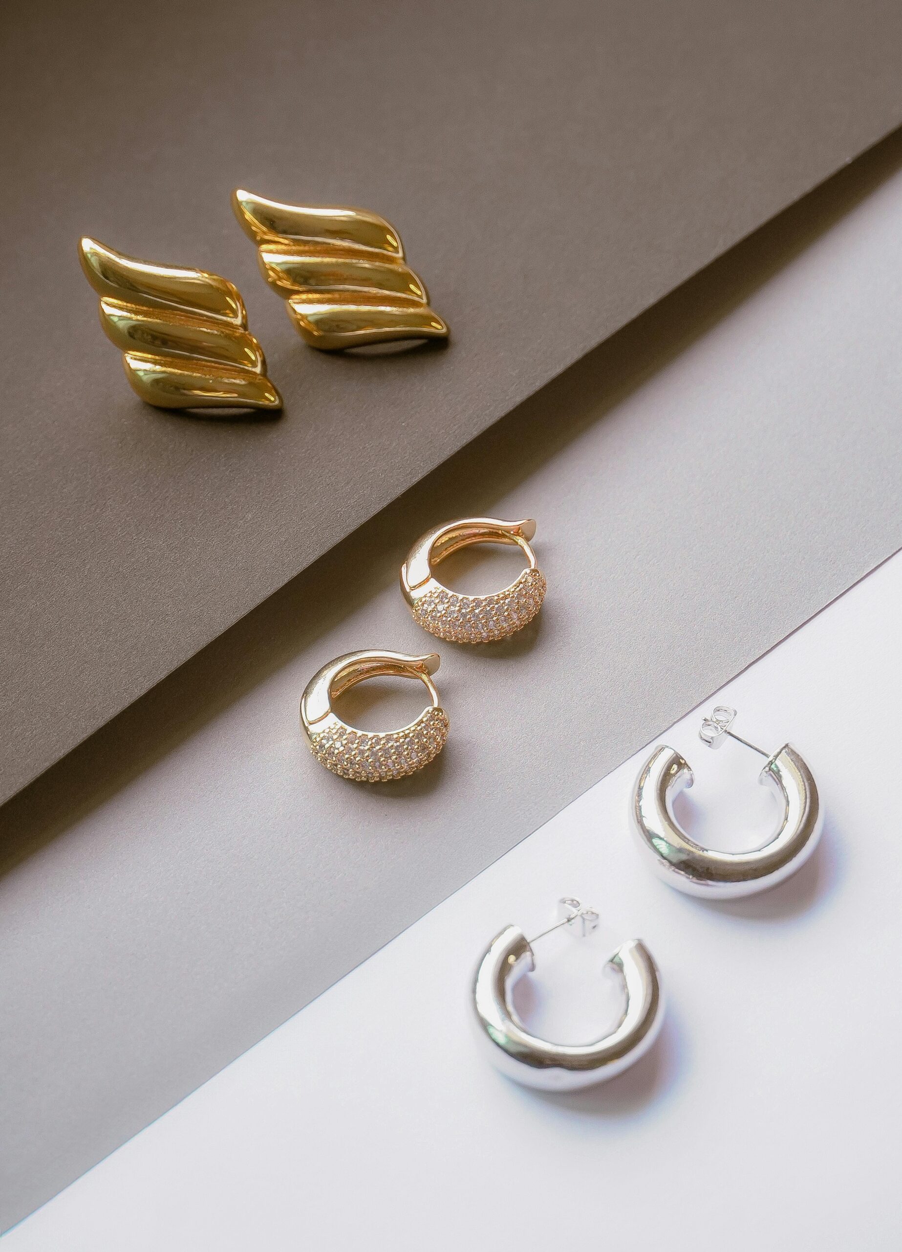 Chic assortment of gold and silver earrings on contrasting backgrounds, showcasing modern jewelry design.