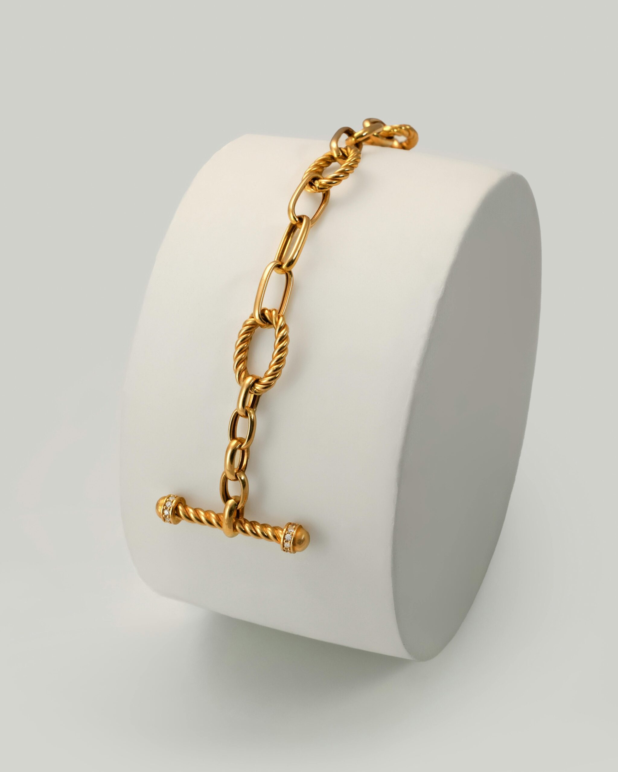 Sophisticated gold chain link bracelet on a cylindrical display, perfect for luxury fashion.