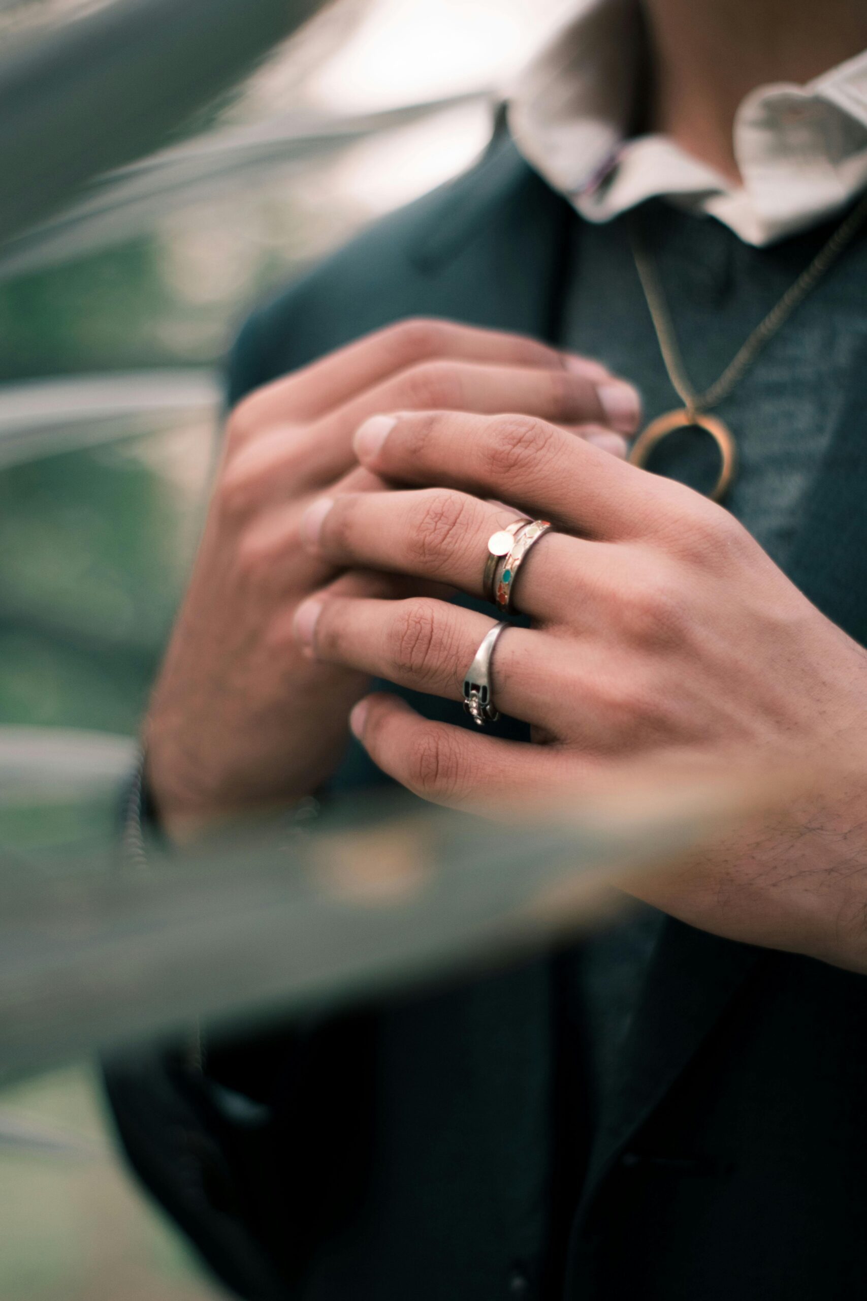 Close-up image of hands with multiple rings and a necklace, wearing a suit.