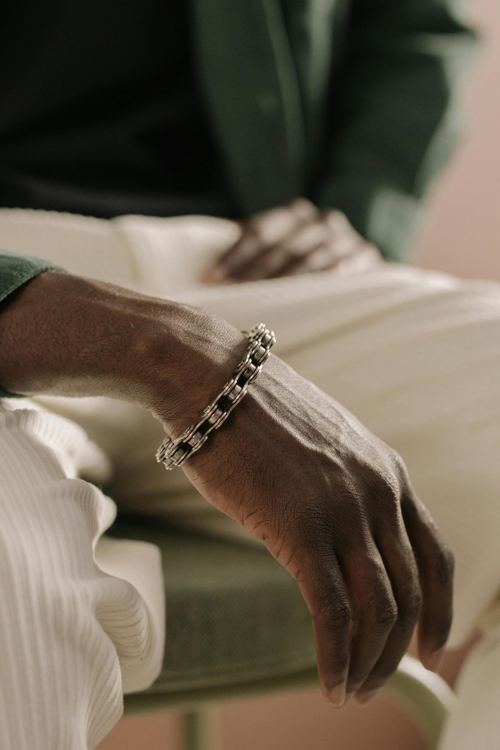 Close-up of a stylish silver bracelet on a man's hand resting on his knee.