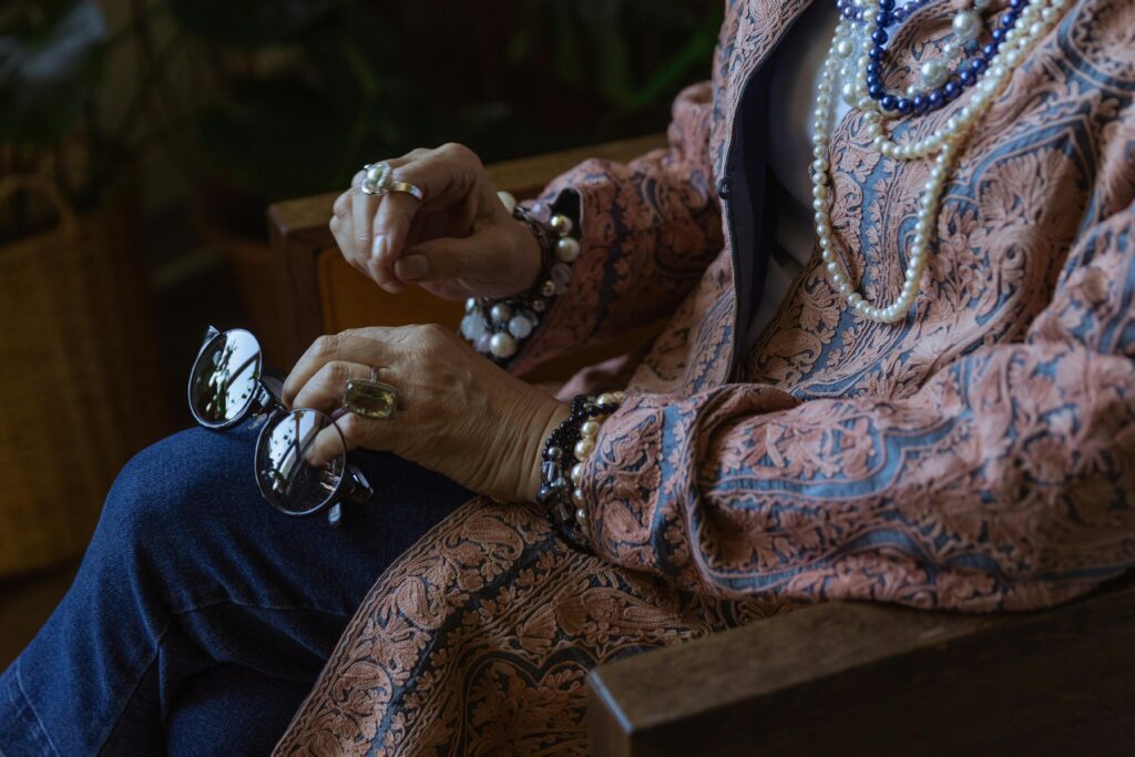 An elderly woman elegantly adorned with jewelry and holding eyeglasses, showcasing boho style.