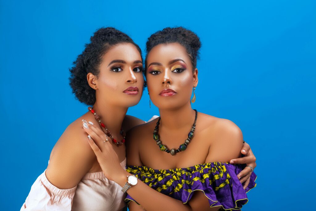 Two beautiful women in elegant outfits and jewelry posing against a blue background.