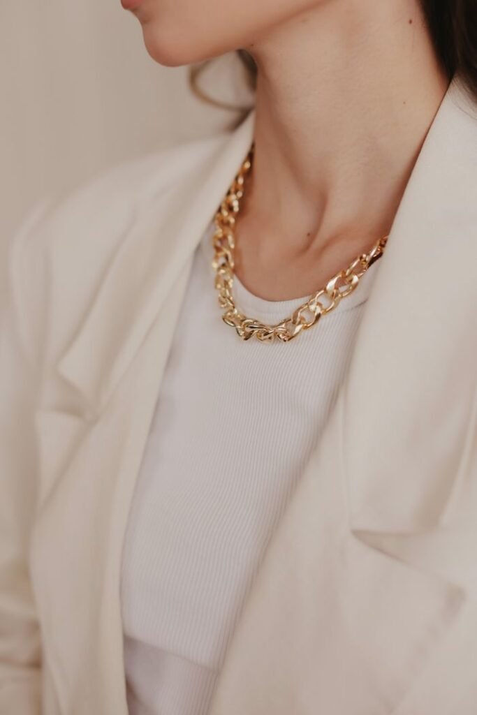 Stylish gold chain necklace worn with a white blazer, exuding elegance.