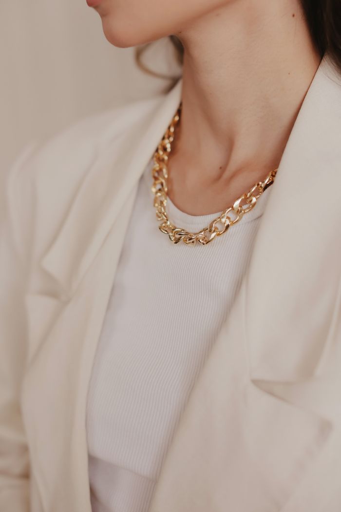 Stylish gold chain necklace worn with a white blazer, exuding elegance.